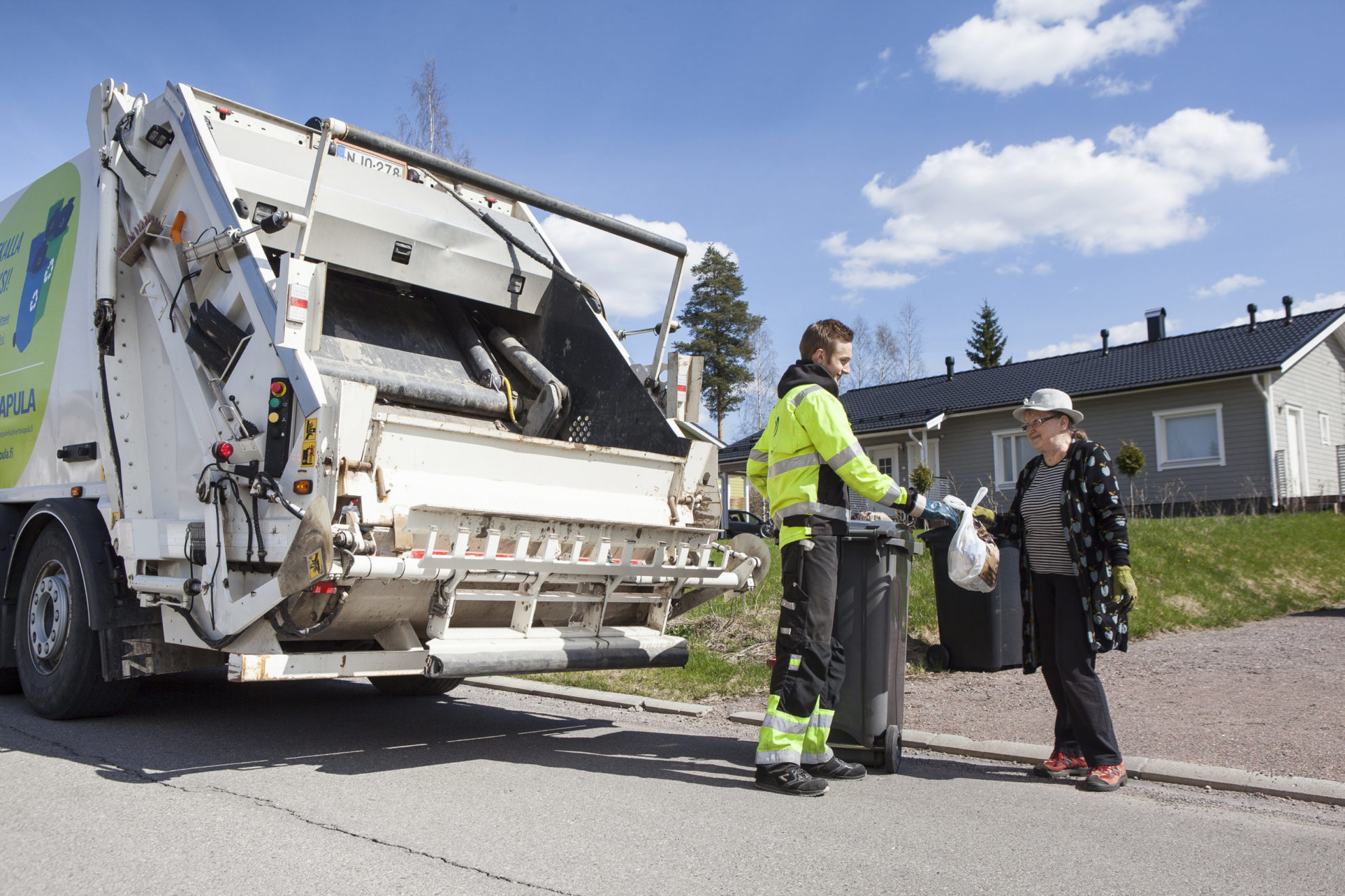 Asukas ojentaa roskapussin jäteautonkuljettajalle